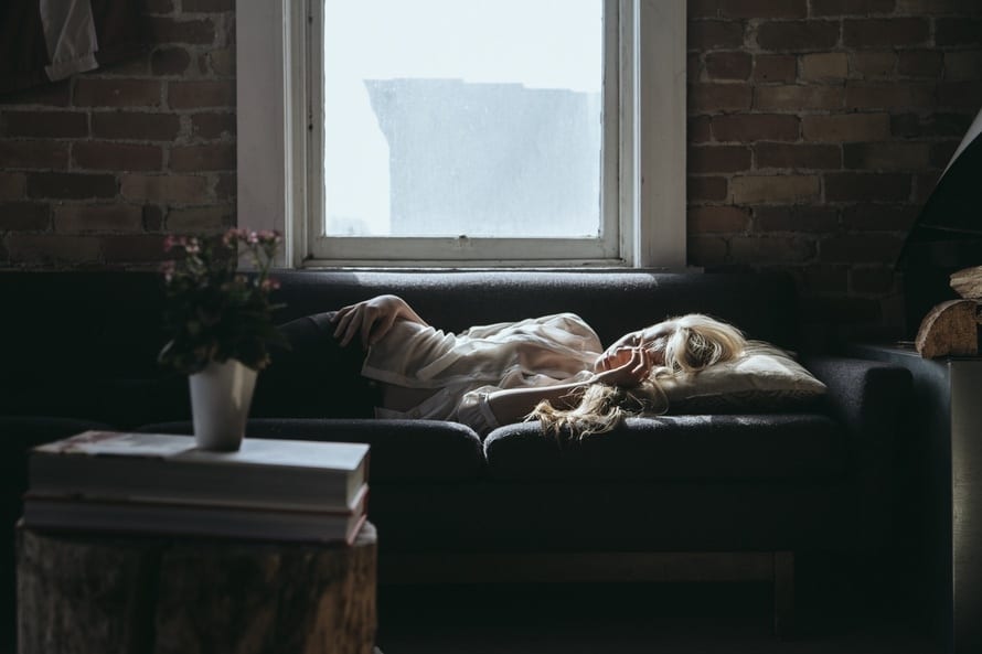 A woman resting on a sofa beside a window